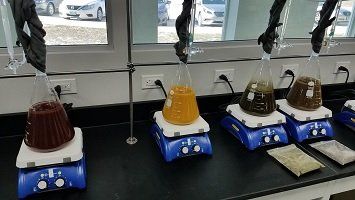 Flasks on hot plates with different colored liquids in a lab setting. Each flask is connected to a condenser.