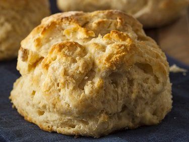 Fluffy, golden-brown biscuit on a blue cloth. Close-up with visible layers and a crispy top.