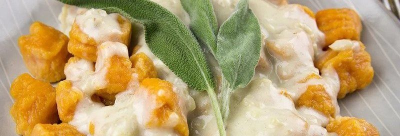 Gnocchi with creamy sauce and fresh sage on a white plate. The gnocchi is orange, and the sauce is white.