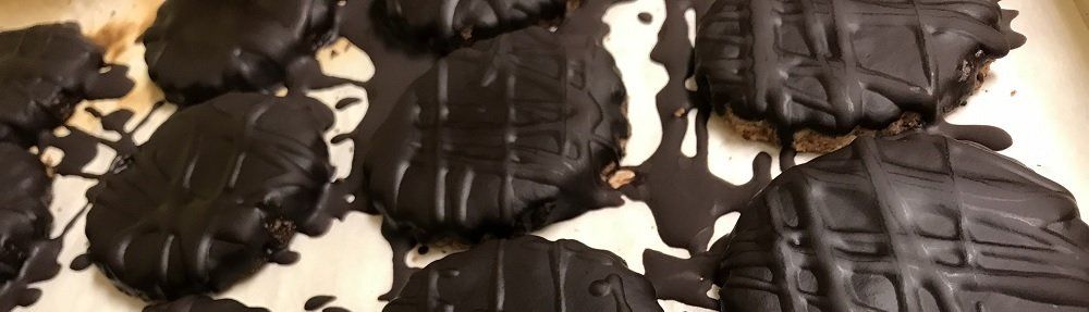 Close-up of chocolate-covered cookies drizzled with melted chocolate on a light-colored surface.