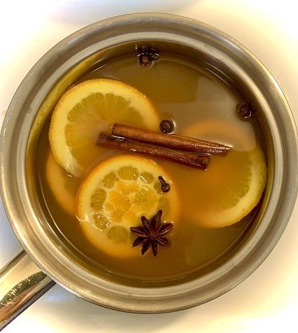 A pot of simmering orange slices, cinnamon sticks, star anise, and cloves. The beverage is golden.