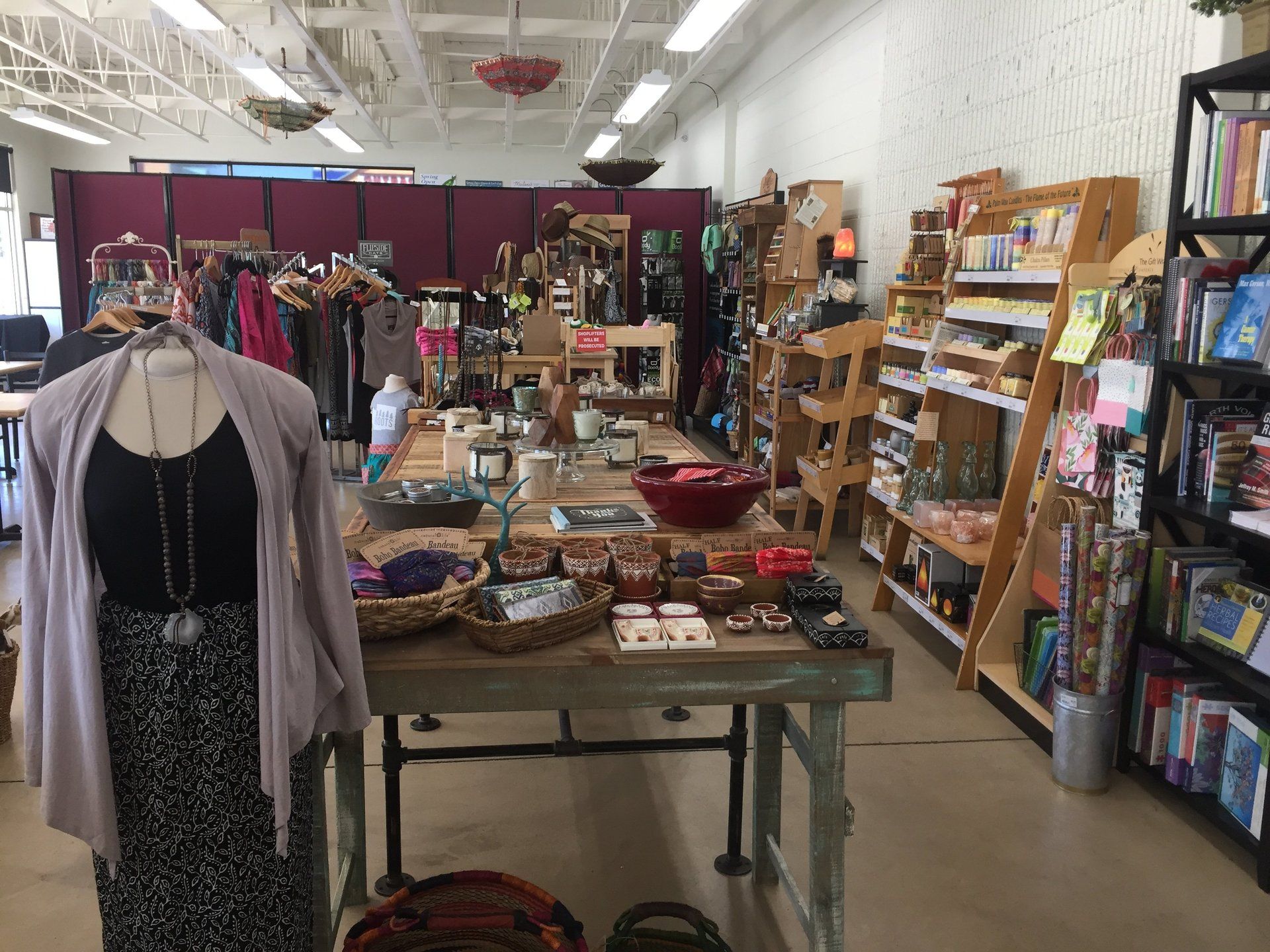 Inside a retail shop with items displayed on tables and shelves. A mannequin wears a gray cardigan and black tank top.