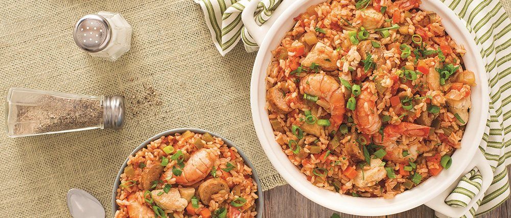 Two dishes of seafood jambalaya with shrimp, in a white serving dish and a smaller tin, with salt and pepper shakers.