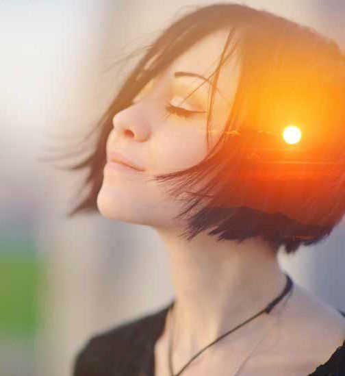 Woman with short dark hair and closed eyes, overlayed with a sunset scene, appearing thoughtful.