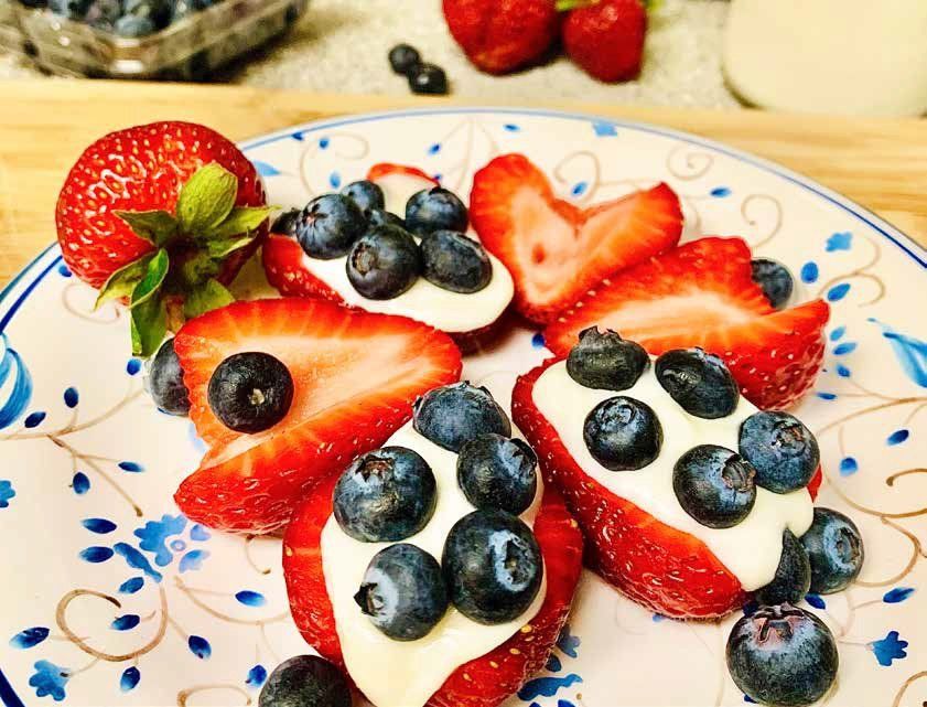 Strawberries filled with white cream and topped with blueberries on a blue and white patterned plate.