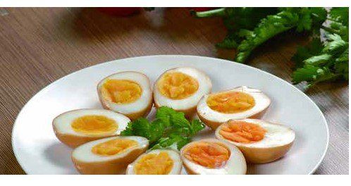 A plate of halved brown-stained eggs with bright orange yolks and white egg whites, garnished with green leaves.