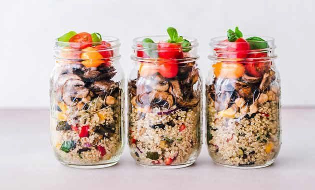 Three mason jars filled with colorful quinoa salad topped with tomatoes and basil sprigs.