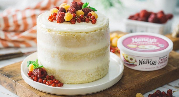 Cake decorated with berries and cream cheese container on a wooden board.
