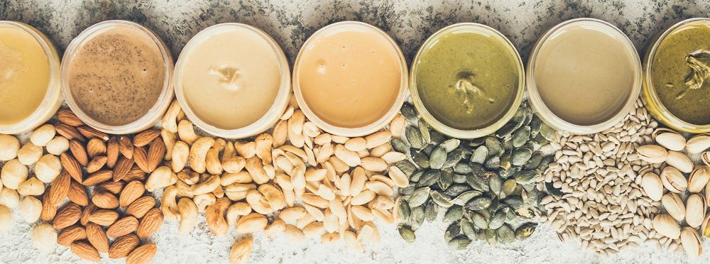 Bowls of nut and seed butters arranged with their corresponding ingredients.