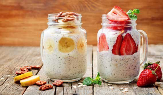 Two jars of overnight oats, one with bananas and pecans, the other with strawberries, sitting on a wooden table.