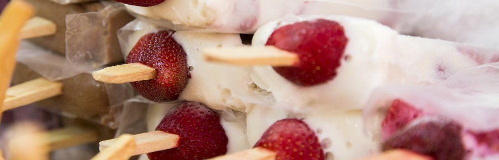 Close-up of white ice pops with strawberries and wooden sticks. Some pops are melting.