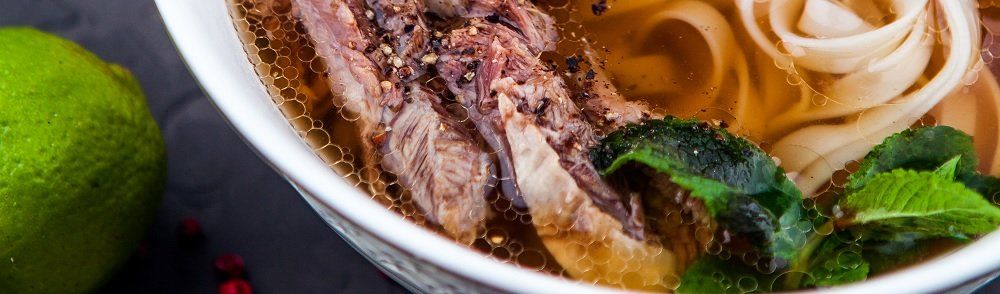Bowl of pho with beef, noodles, herbs, and a lime on the side.