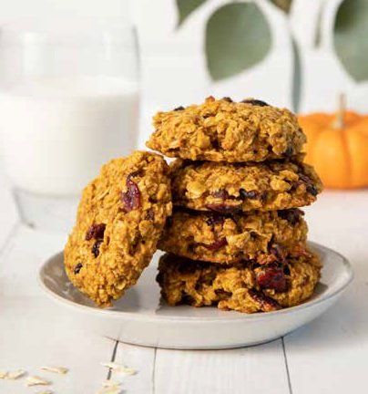 Stack of pumpkin oatmeal cookies on a plate next to a glass of milk and a small pumpkin.