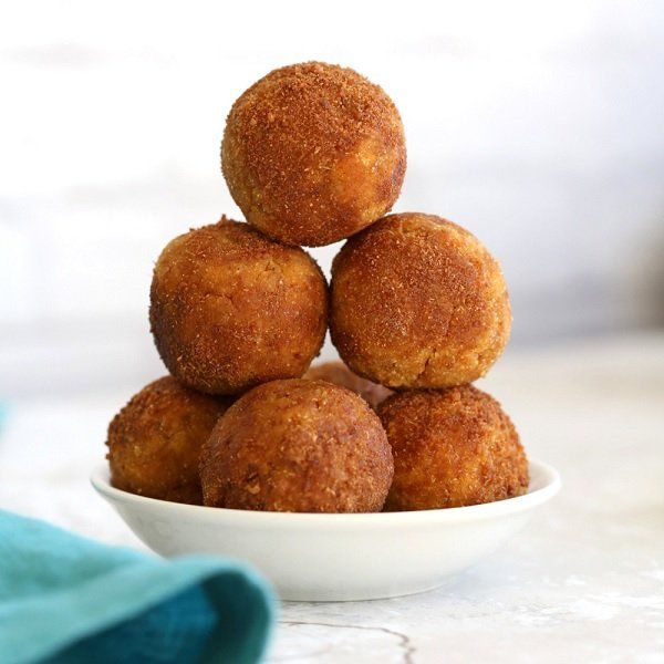 A stack of golden-brown arancini balls in a white bowl, set on a white surface next to a blue cloth.
