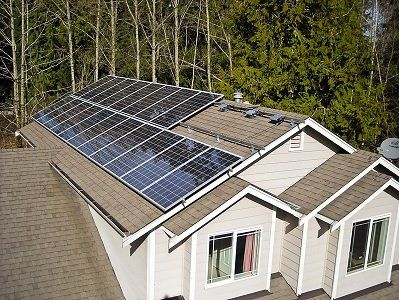 Solar panels installed on a residential rooftop against a backdrop of trees.