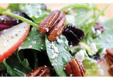 Close-up of a salad with pecans, apple slices, greens, dried fruit, and crumbled cheese.