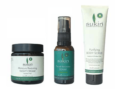 Sukin skincare products: night cream, facial recovery serum, and body scrub. The packaging is white, black, and green.
