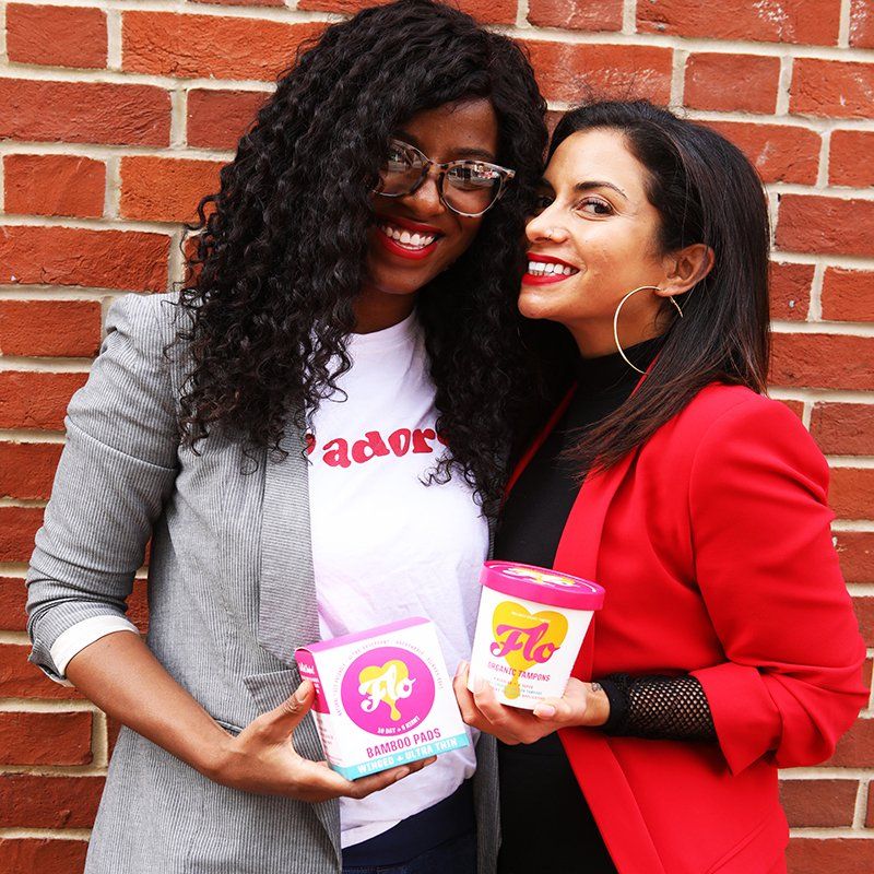 Two women holding ice cream, standing in front of a brick wall. One wears a white shirt with 