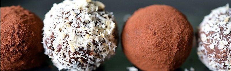 Close-up of four chocolate truffles: two covered in cocoa powder, and two coated in white coconut flakes.