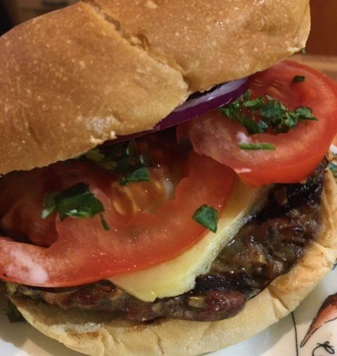 A delicious burger on a bun, with tomato, red onion, and cheese. Sprinkled with herbs.