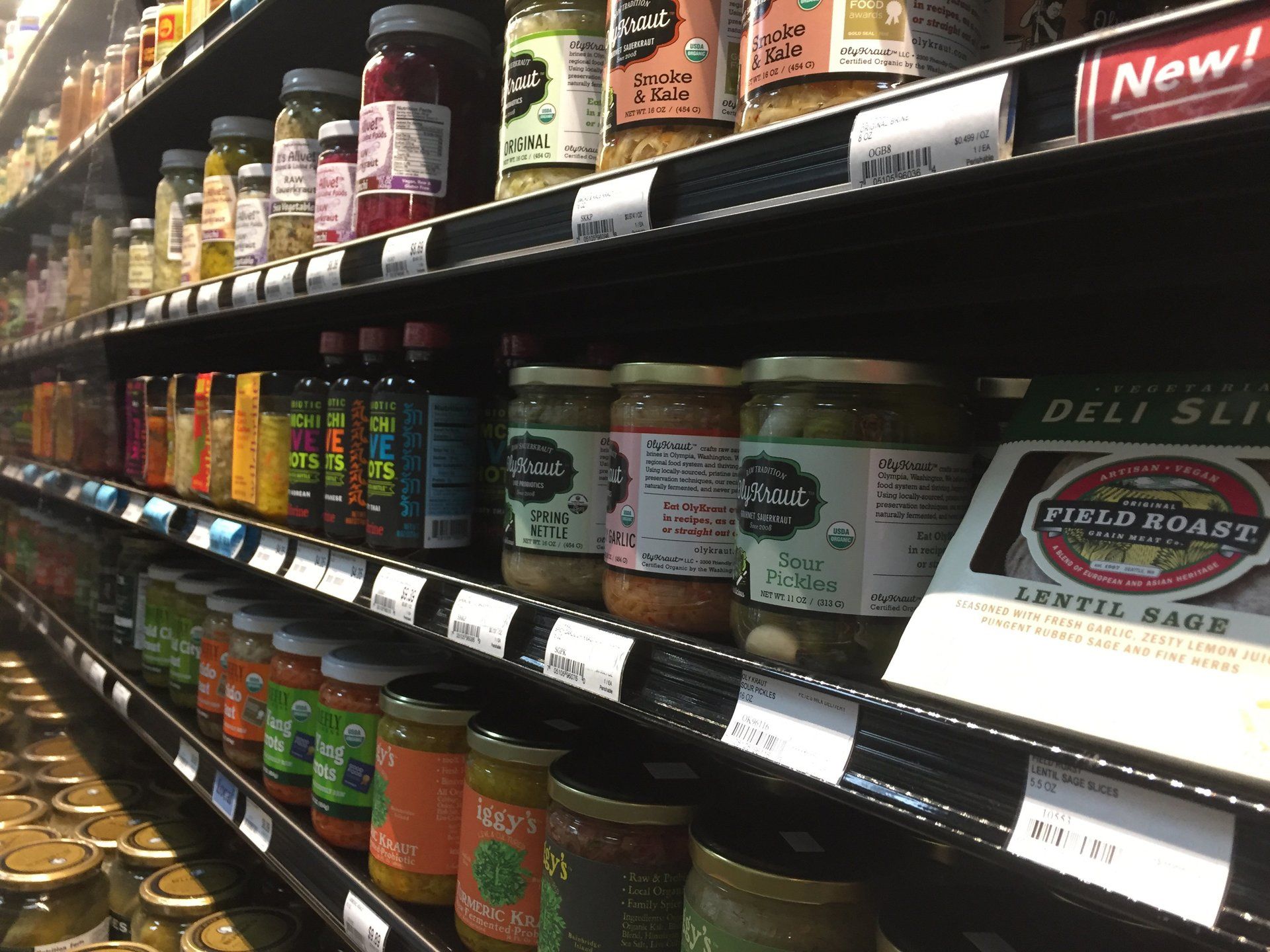 Shelves of jars and bottles with various food products in a grocery store. Includes sauces, pickles, and deli slices.