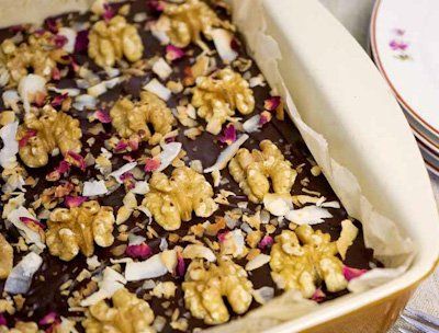 Brownie in a baking dish topped with walnuts, coconut flakes, and pink rose petals.