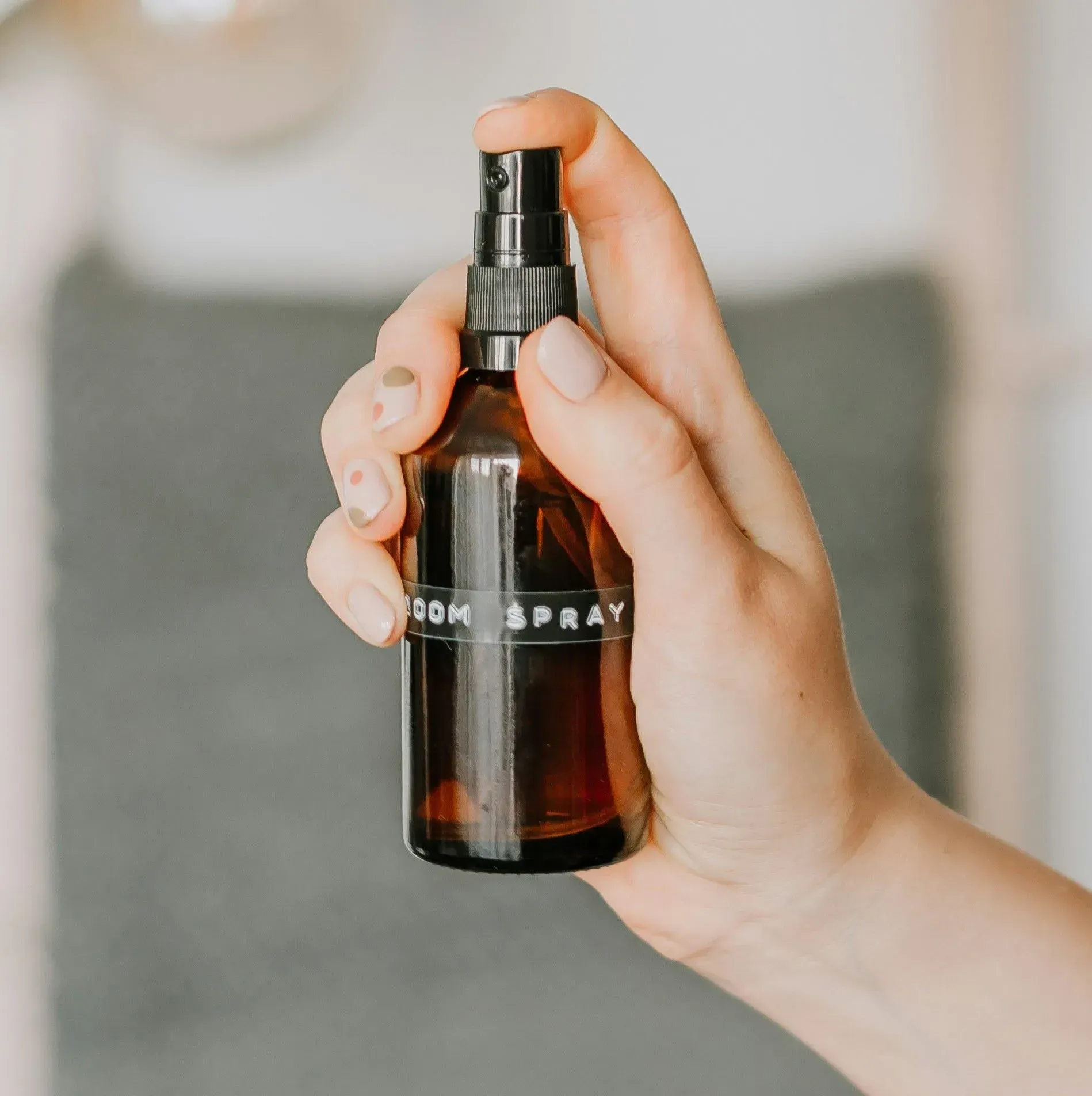 A hand holds an amber-colored glass spray bottle labeled 