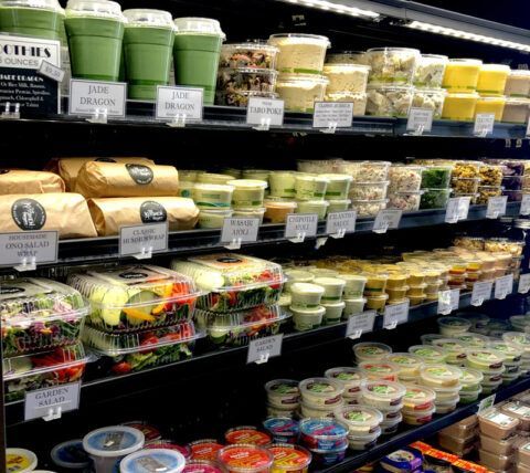 Shelves in a grocery store display pre-packaged green smoothies, salads, wraps, and side dishes.