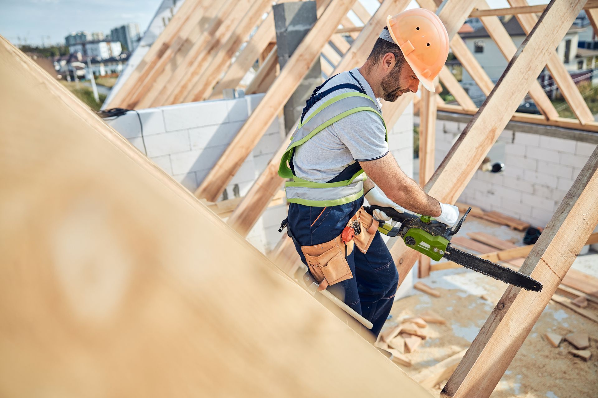 A certified builder using a chainsaw at a construction site with timber and cement blocks.