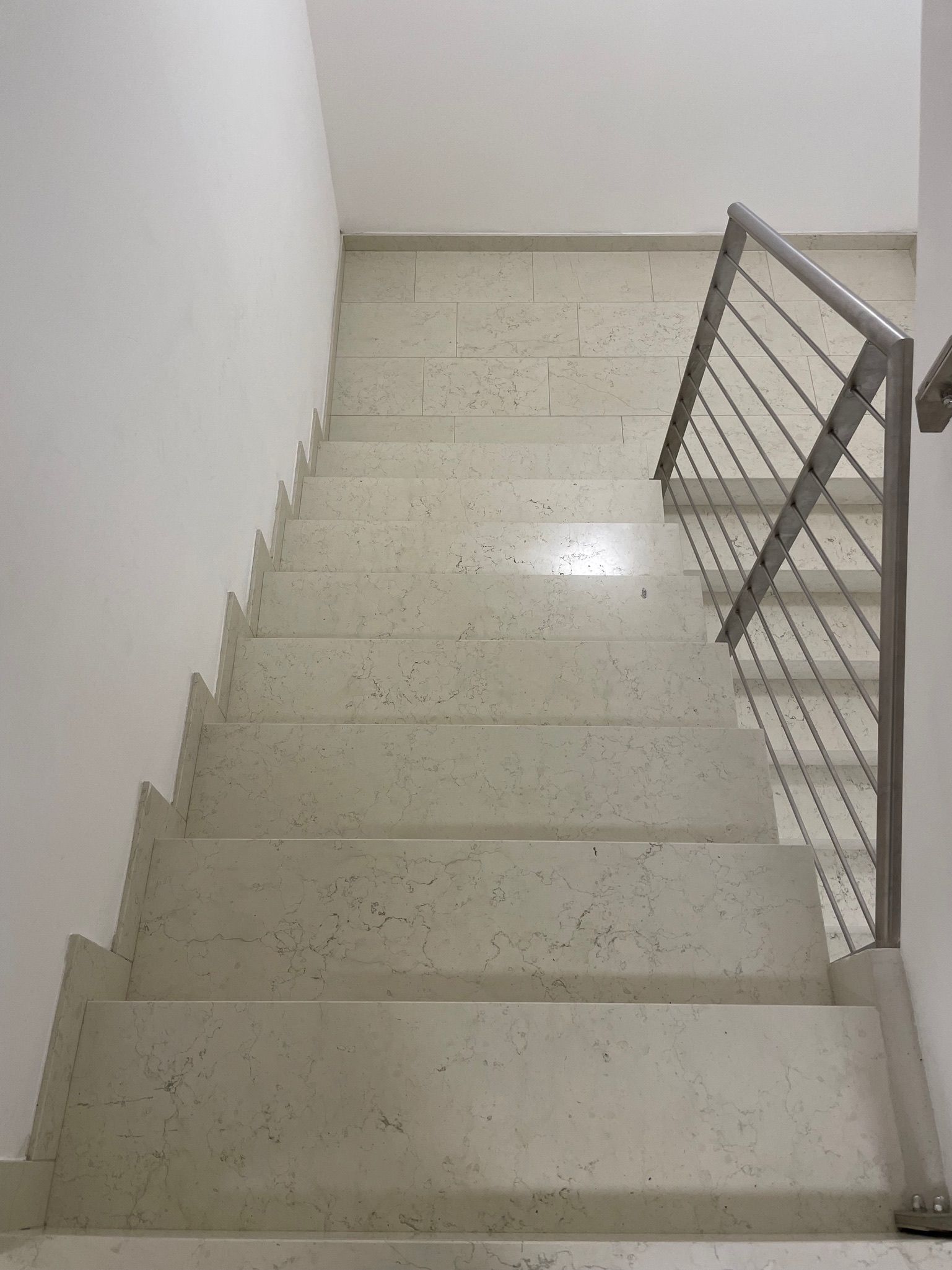 Vano scale interno con gradini in piastrelle chiare e ringhiera in metallo sulla destra.