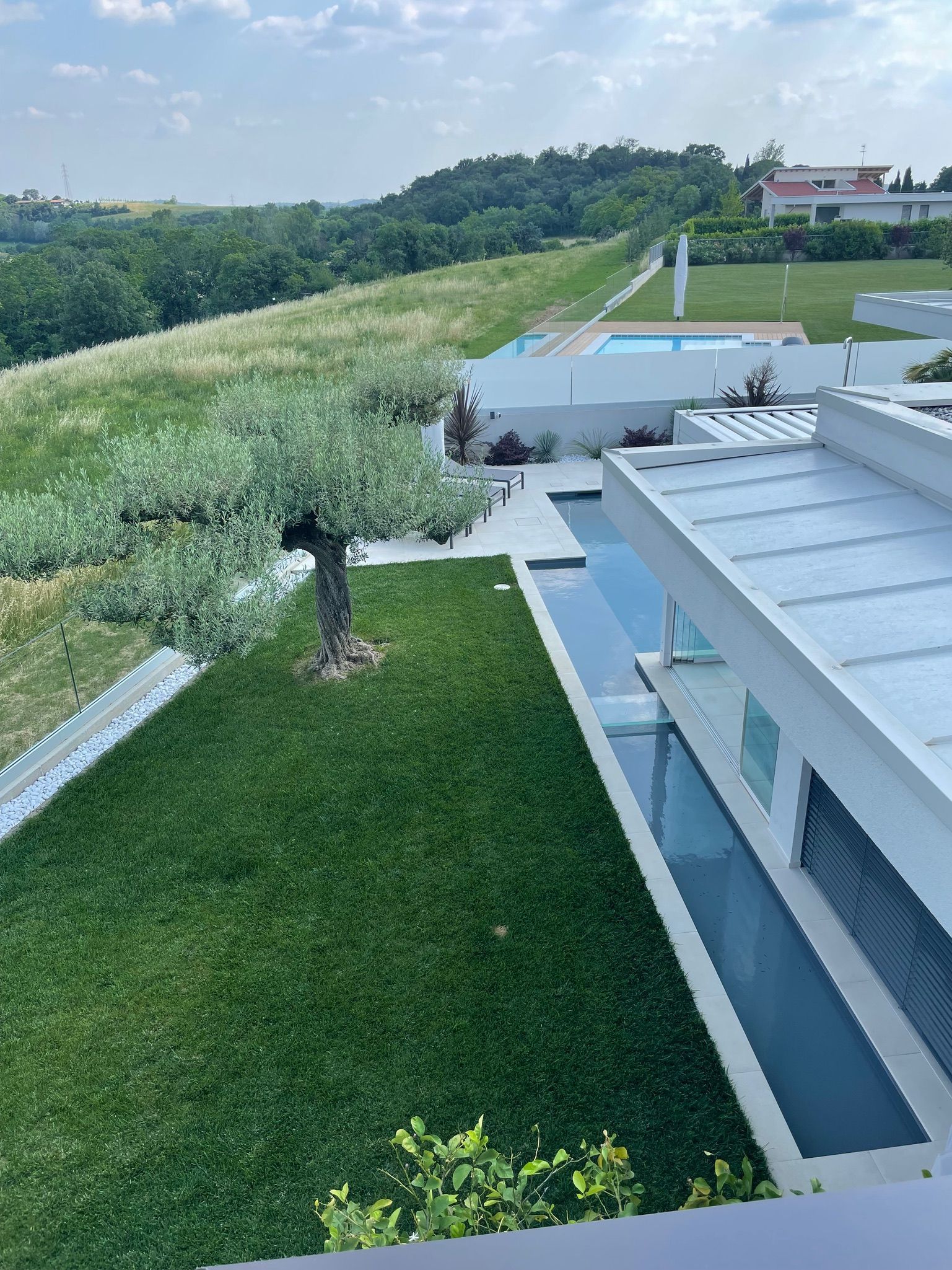 Moderno edificio bianco accanto a un prato verde e ad alte erbe su un pendio sotto un cielo nuvoloso