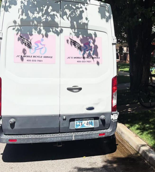 White van with pink bicycle service logo, parked on a street.