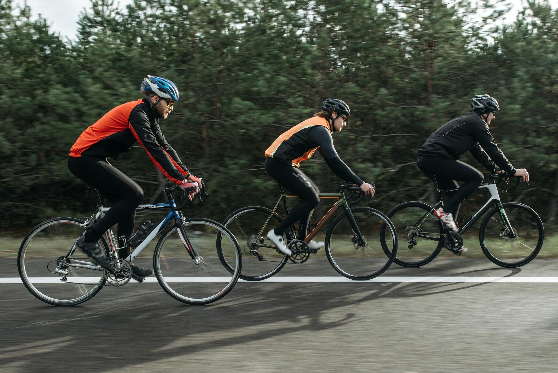 Three cyclists in sporty attire riding on a road, trees in the background.