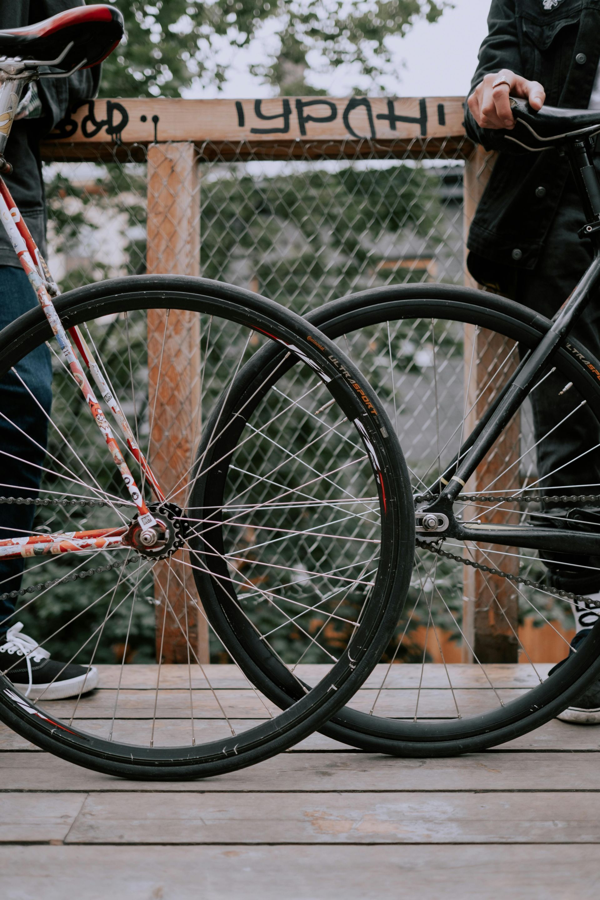 Two bicycles with intersecting wheels; people leaning on a bridge railing.