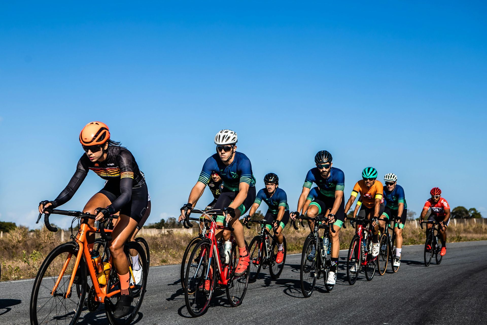 Cyclists in colorful jerseys ride on a road under a blue sky.