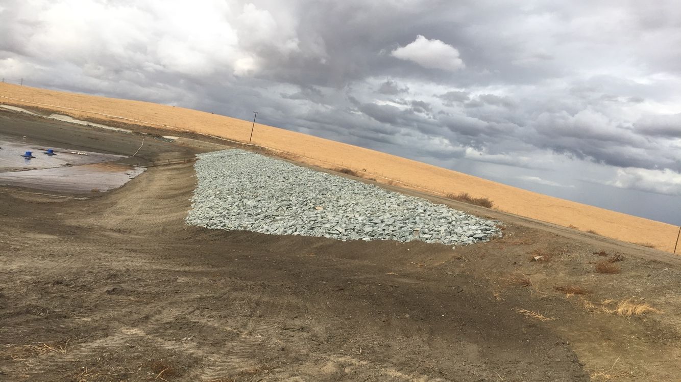 A rocky retaining wall on a hillside under a cloudy sky.