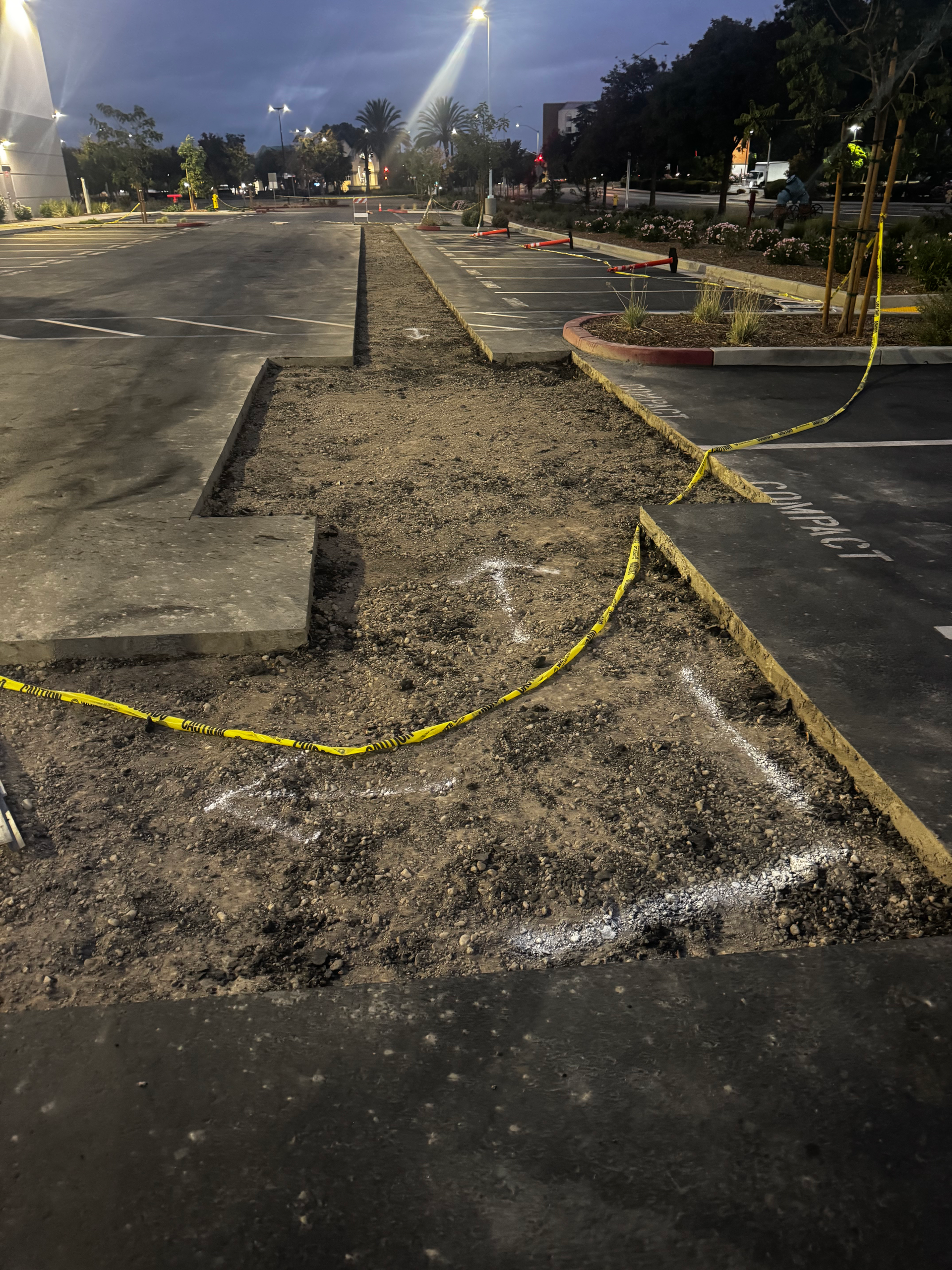 Parking lot under construction, with exposed gravel and marked areas, barricaded with yellow tape.