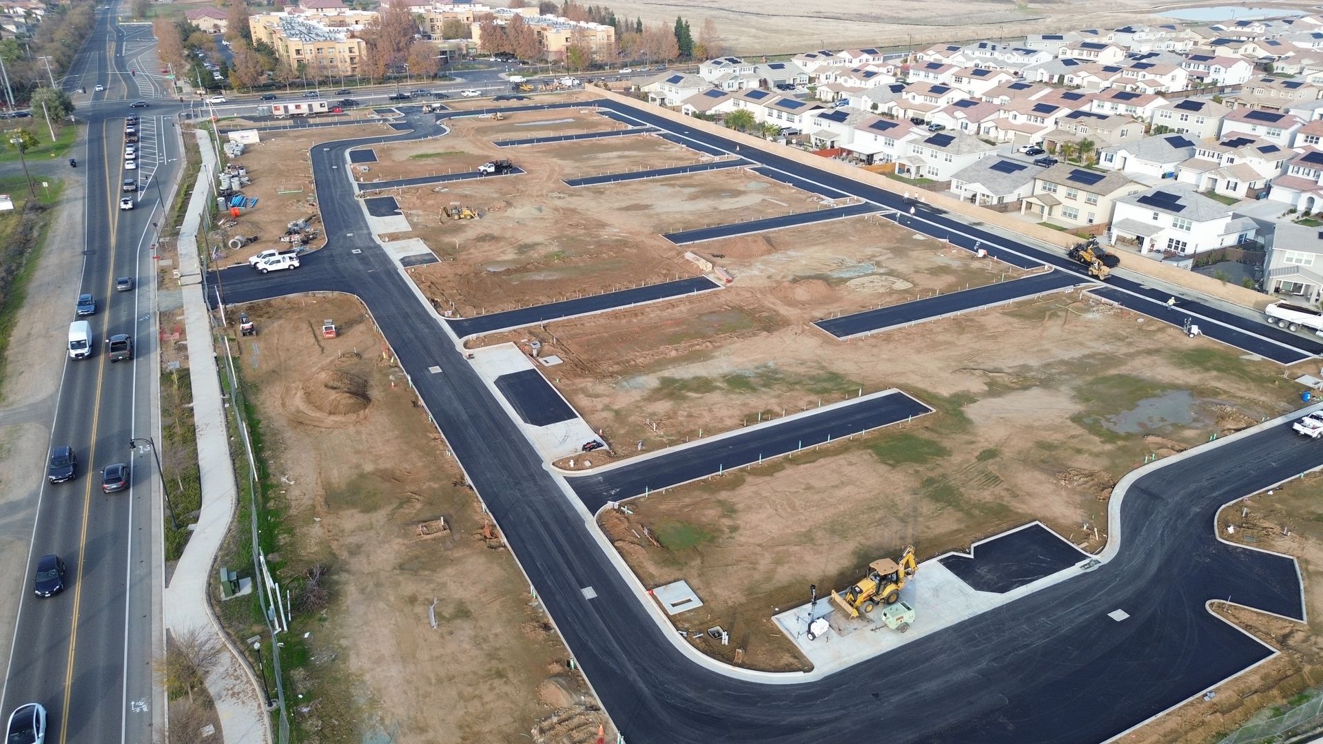 Aerial view of a new residential construction site with graded plots, roads, and completed homes nearby.
