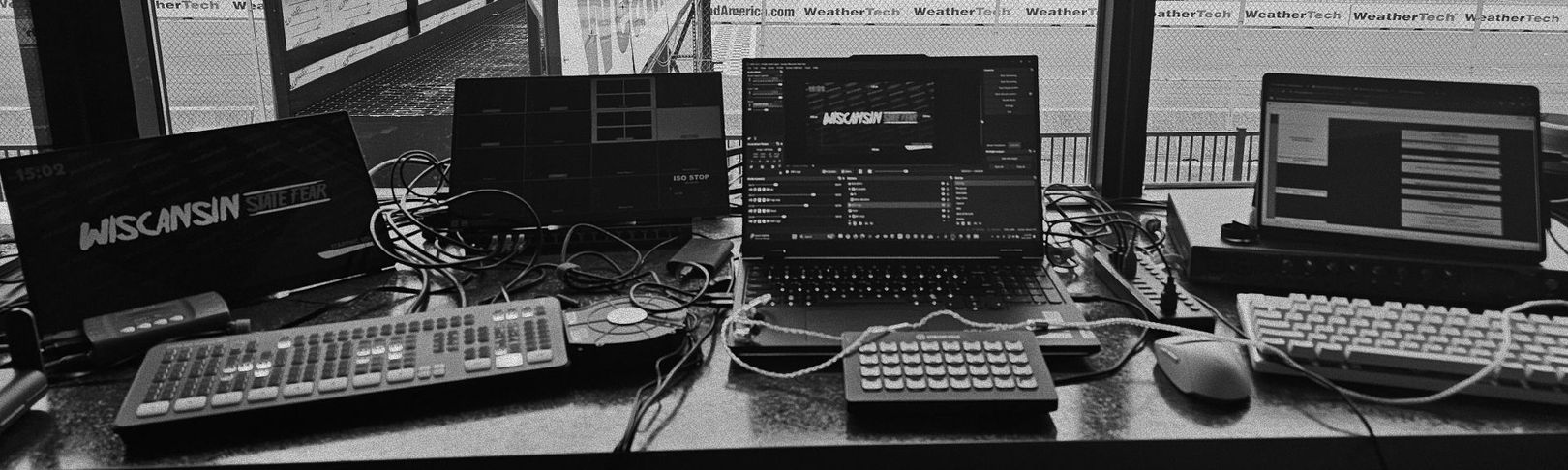 A desk with multiple laptops, keyboards, and equipment, likely used for data analysis or control, near a window.