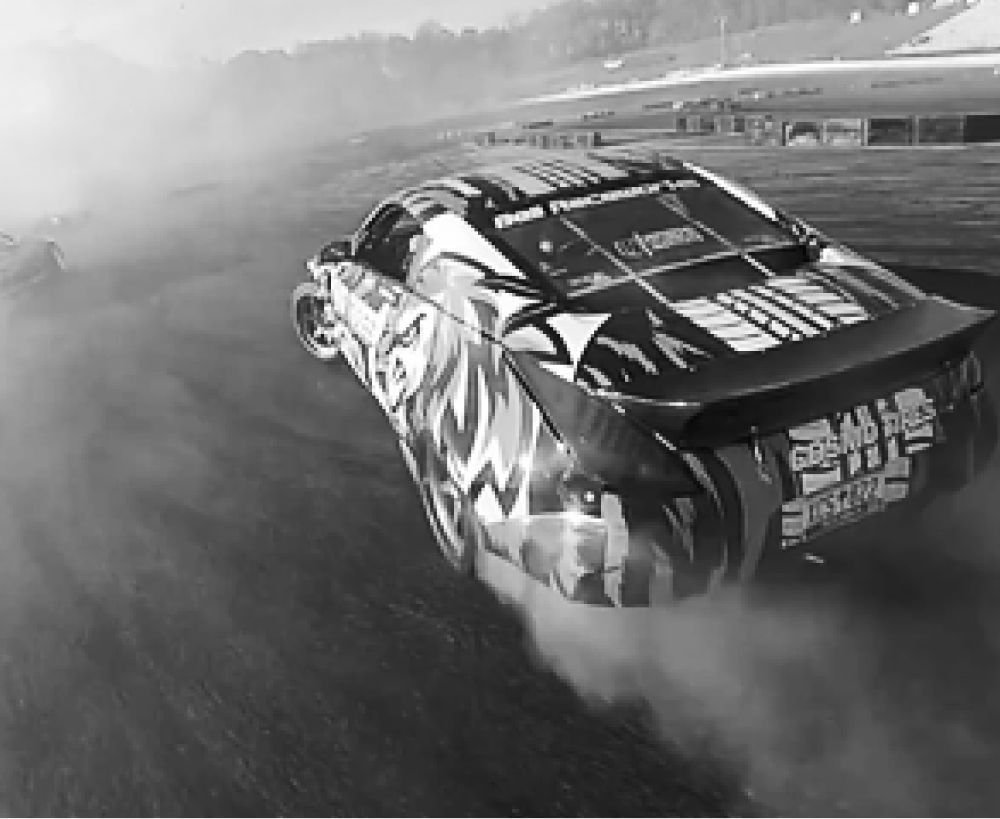 Drifting car, rear view, in motion, generating smoke on a race track.