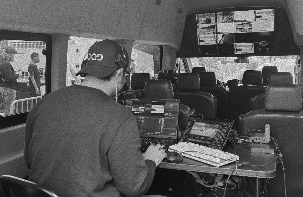 Inside a production truck: Operator works at a desk, monitors show video feeds, and team members are outside on set.