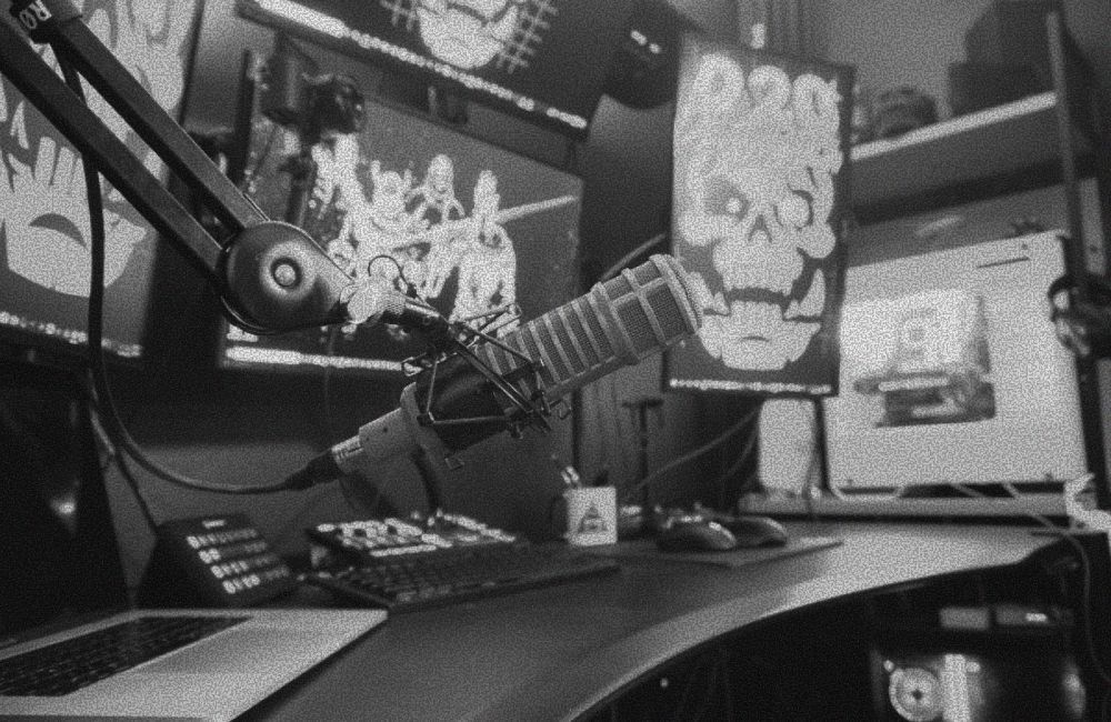 A podcasting setup with a microphone, multiple monitors, and a skull-themed graphic in black and white.