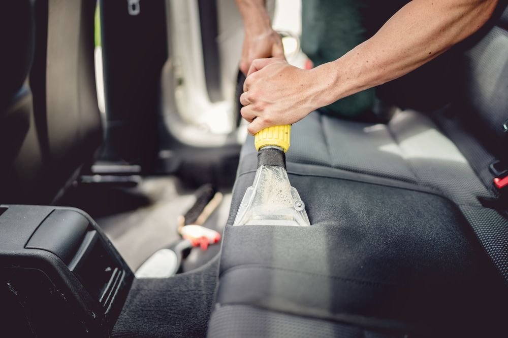 A Man Is Cleaning The Back Seat Of A Car With A Vacuum Cleaner — Pinnacle Carpet & Upholstery Cleaning In Central Coast, NSW