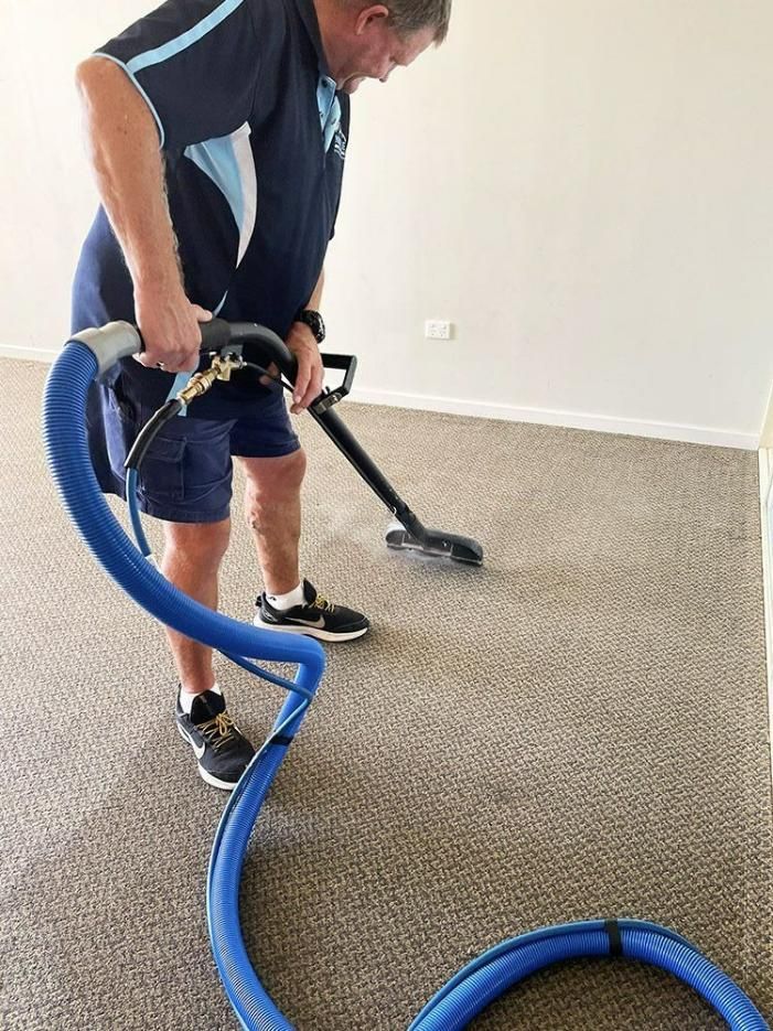 A Man Is Cleaning A Carpet With A Vacuum Cleaner — Pinnacle Carpet & Upholstery Cleaning In Wyong, NSW