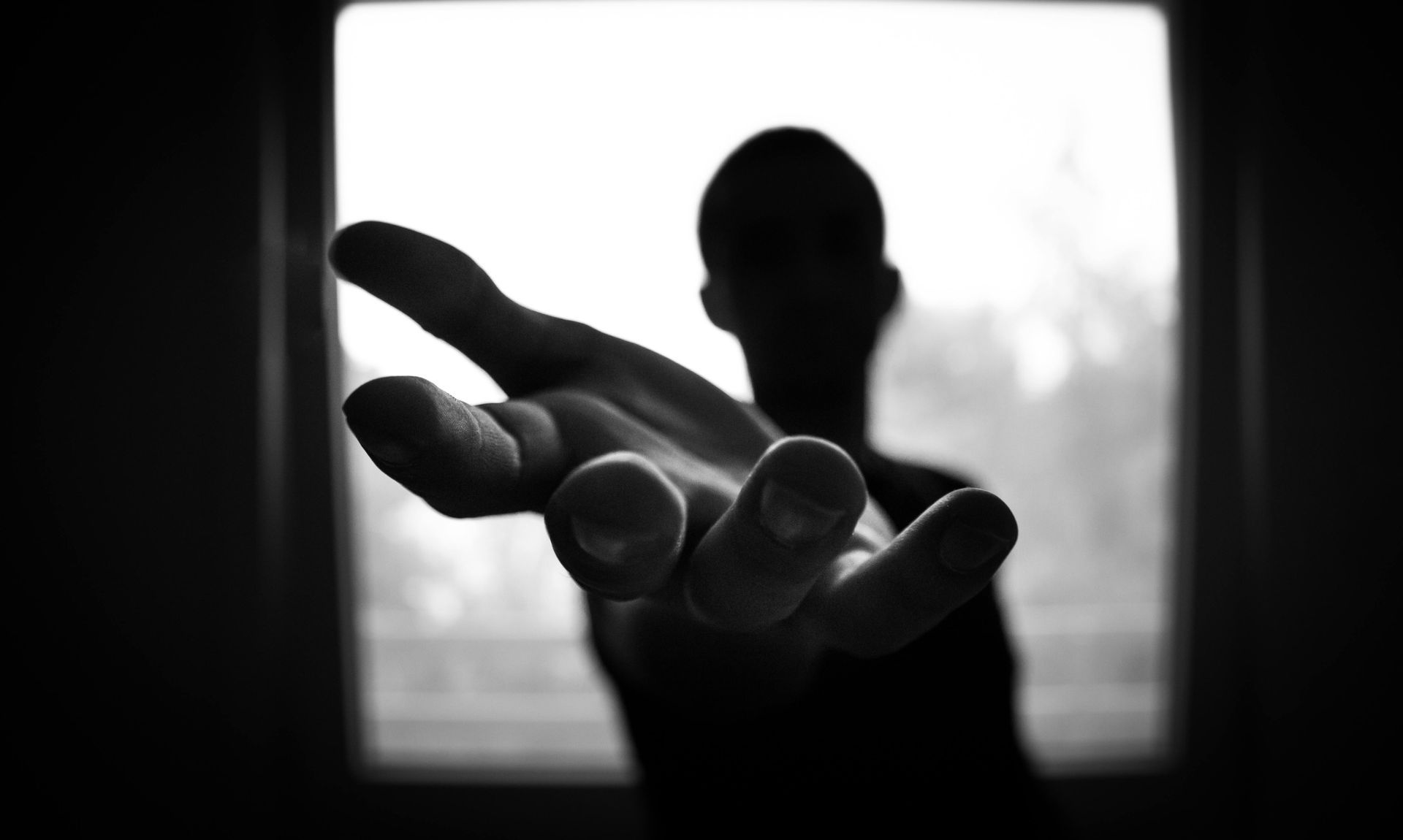 hand reaching out from an unknown person framed by a window with blurry city scape