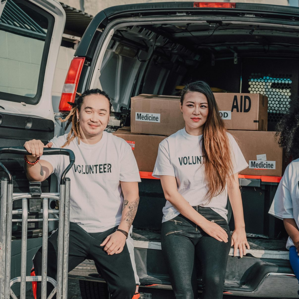 Two volunteers resting on the back of a cargo van with boxes labeled AID