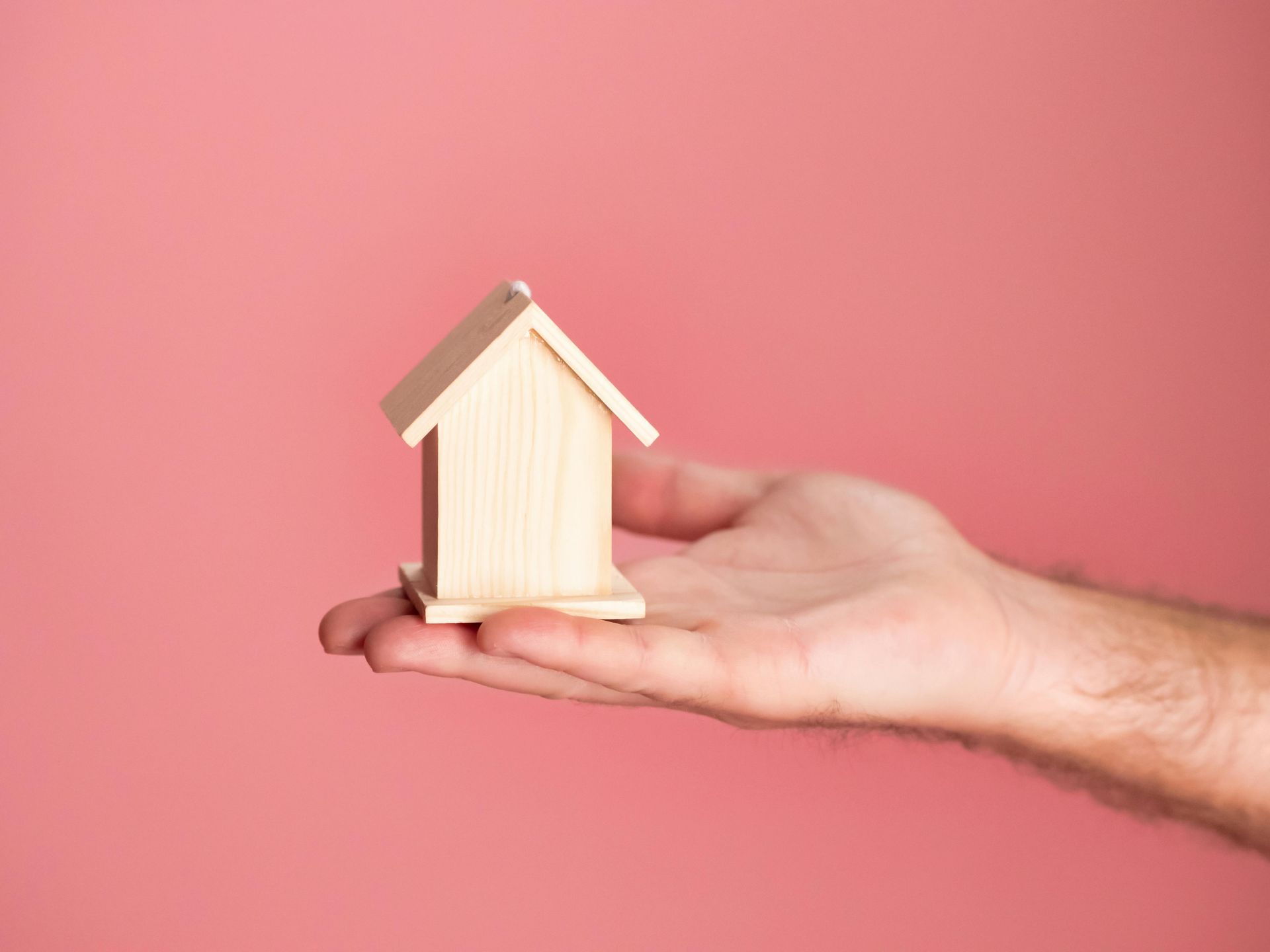 wooden house held in someone's palm against a pink background