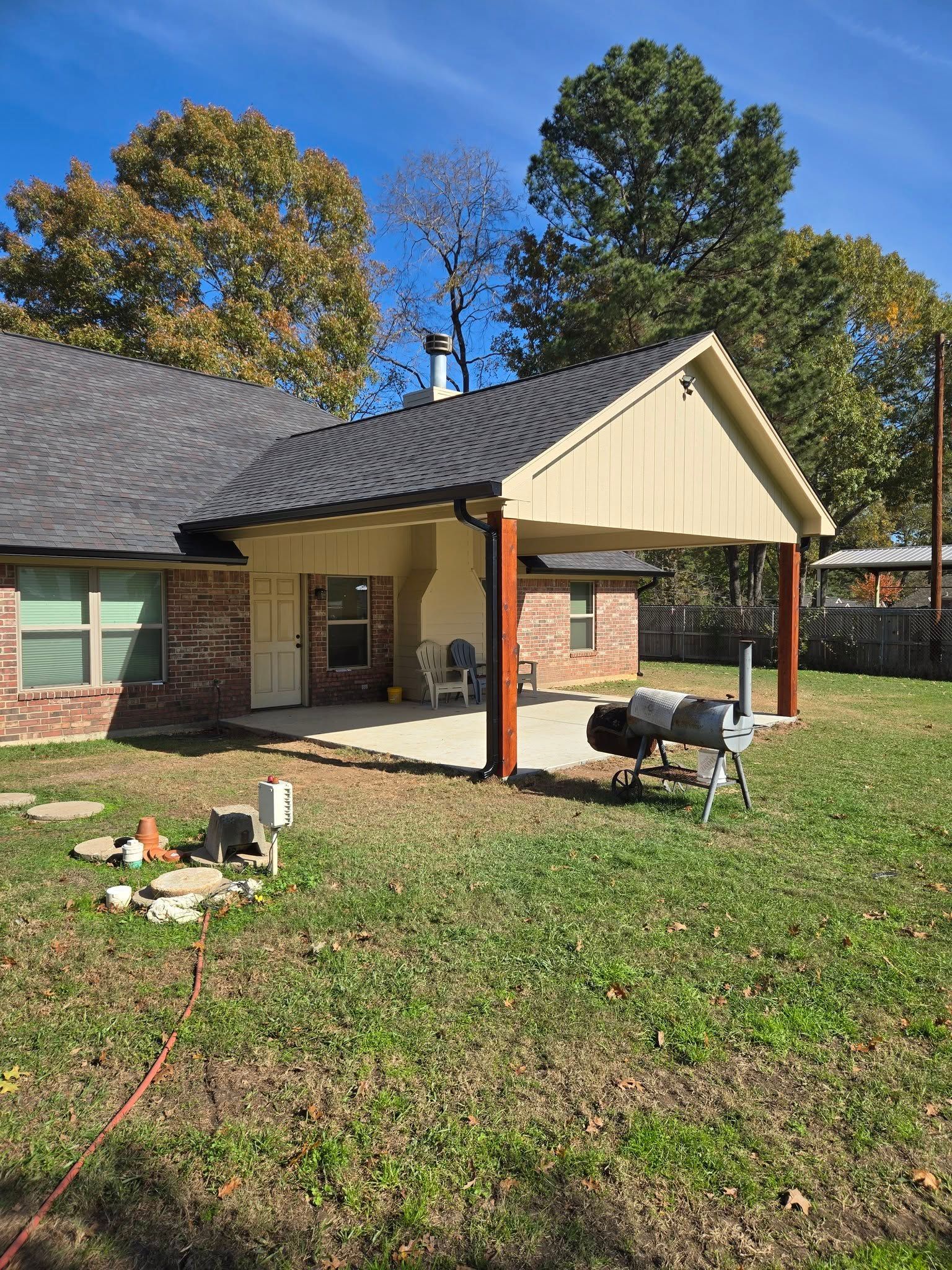 A house with a covered patio and a grill in the backyard.