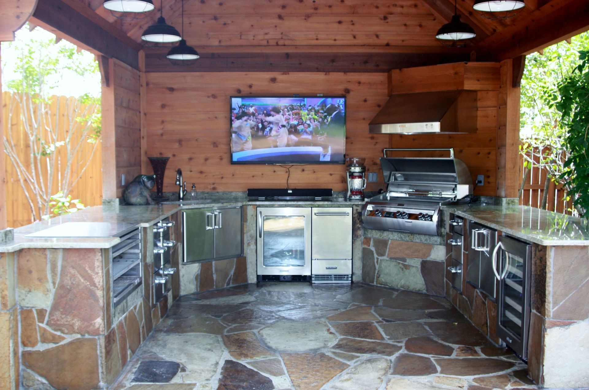 A large outdoor kitchen with a television mounted on the wall.