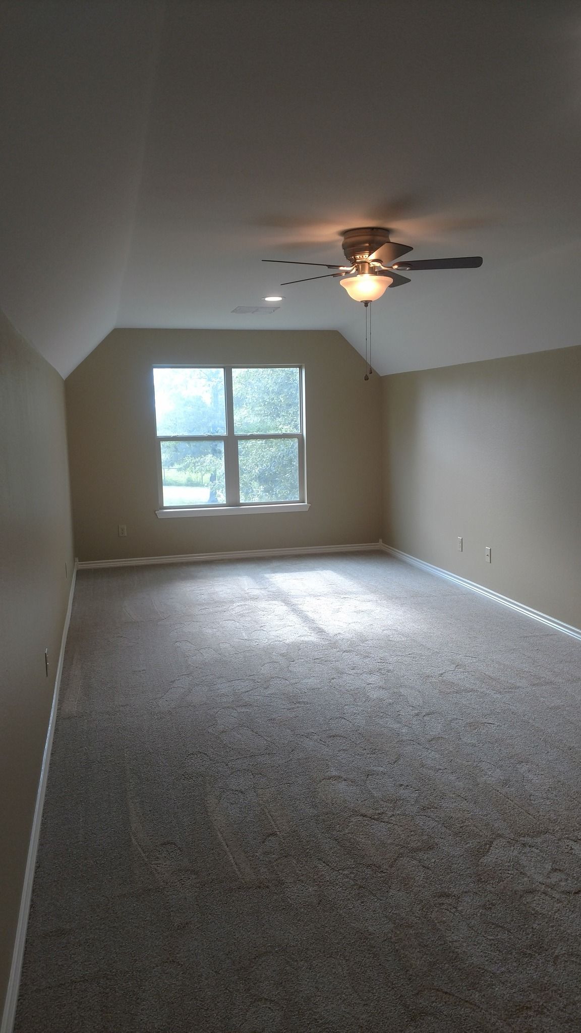 An empty room with a ceiling fan and a window.